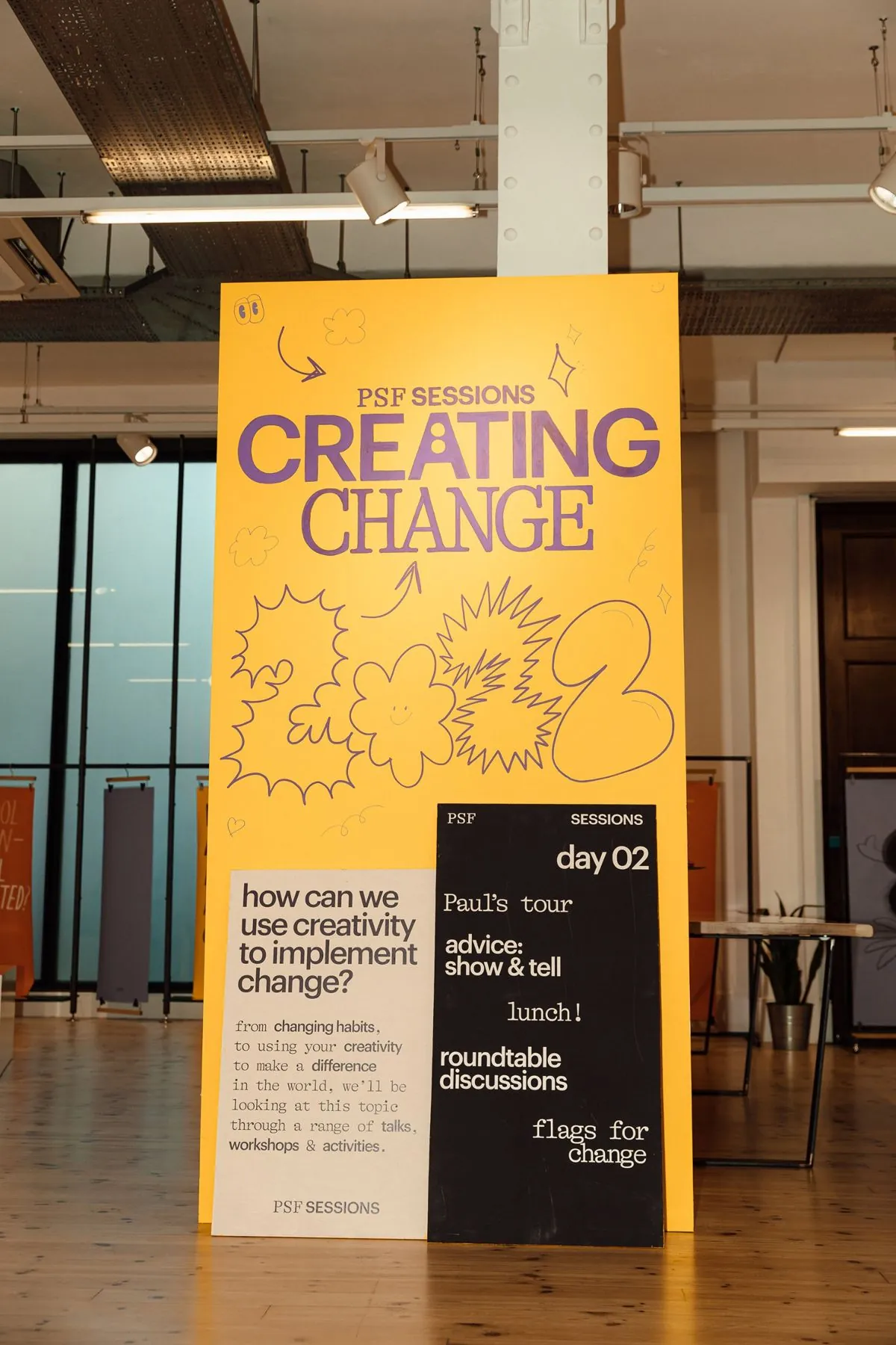 &ldquo;Creating Change&rdquo; yellow hand-painted board with day 02 programme